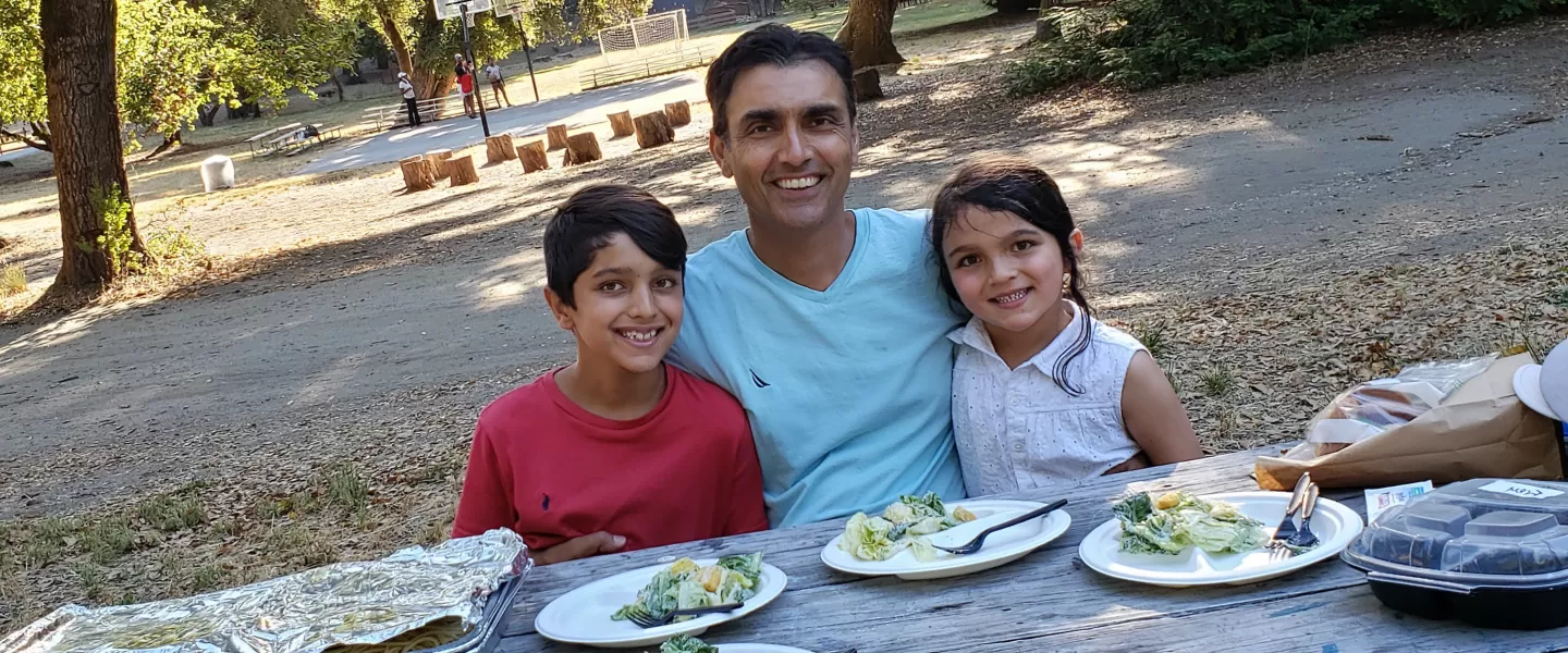 Dad and two kids smiling and munching on dinner at the picnic table
